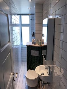 a white toilet sitting next to a sink in a bathroom under a window on top of a tiled floor