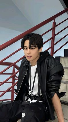 a young man sitting on the steps wearing a black jacket and white t - shirt