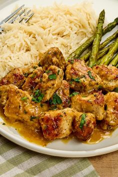 a white plate topped with chicken and asparagus next to rice on a table