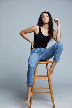 a woman sitting on top of a wooden stool with her hand on her hip and looking at the camera