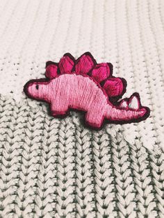 a pink dinosaur embroidered onto the side of a white knitted blanket