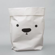 a white paper bag with a black face on the front and bottom, sitting on a gray surface