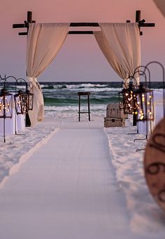 an outdoor ceremony set up on the beach with candles and drapes draped over it