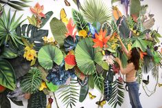 a woman standing next to a wall covered in lots of green and orange leaves with butterflies on it