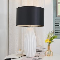 a white table lamp sitting on top of a desk next to a vase with yellow flowers