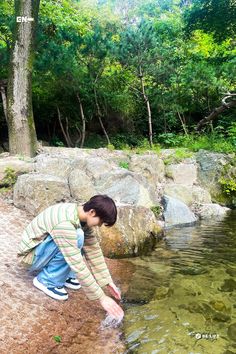 a young boy is playing in the water near some rocks and trees with his feet in the water