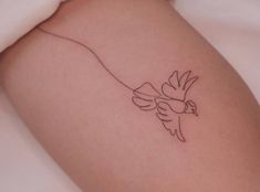 a small tattoo on the back of a woman's thigh with a bird flying above it