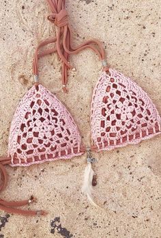 two pink crocheted bras are laying on the sand and one has a tassel