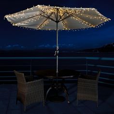 an umbrella is lit up on top of a table with chairs and tables underneath it