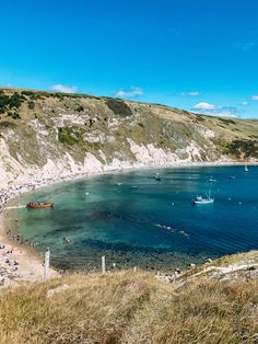 the beach is crowded with people and boats in the blue water near white cliffs on a sunny day