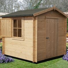 a small wooden shed sitting on top of a lush green field next to purple flowers