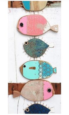 three colorful fish are hanging on a wooden wall and one is painted pink, blue, and green