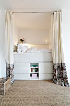 a white bed sitting under a window next to a book shelf