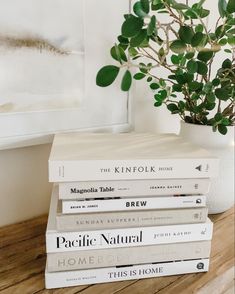 a stack of books sitting on top of a wooden table next to a potted plant