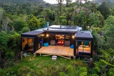 a house made out of shipping containers in the middle of some trees and grass with lights on