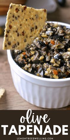 a white bowl filled with olive tapenade and a cracker in the middle