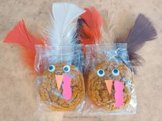 two cookies in plastic bags with fake turkeys on them and feathers sticking out of their mouths