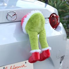 a green stuffed animal hanging from the trunk of a car with santa's hat on it