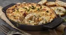 a casserole dish with meat and vegetables in it on a table next to bread