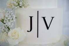 a wedding cake with white flowers and the letter jv on it's side