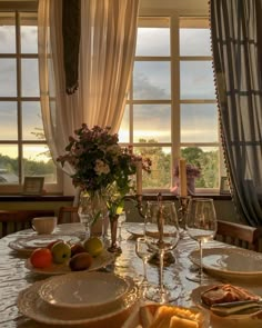 a dining room table with plates and glasses on it, in front of large windows