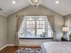 a bedroom with a large window seat next to a bed in front of a chandelier