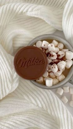 a cup filled with marshmallows on top of a white blanket next to a chocolate bar