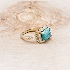 a gold ring with a turquoise stone surrounded by diamonds on a wooden background, close up