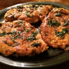 three burger patties with spinach and cheese on a black plate