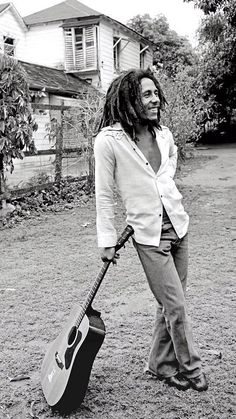 a man with dreadlocks holding a guitar in his hand and standing on the ground