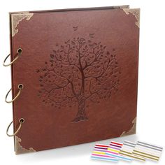 a brown leather book with four colored markers in front of it and an image of a tree on the cover