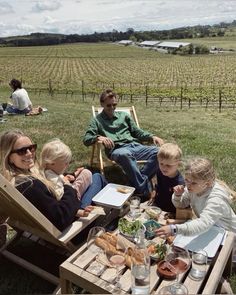 a group of people sitting around a table with food and drinks on it in the grass