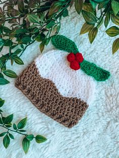 a crocheted hat is laying on a white blanket with green leaves around it