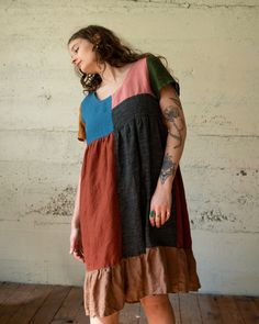 a woman with tattoos standing on a wooden floor wearing a dress that has multicolored panels