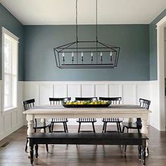 a dining room table and bench in front of a chandelier hanging from the ceiling