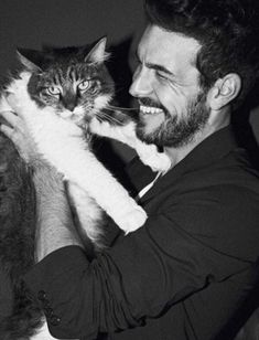 a black and white photo of a man holding a cat in his arms while smiling at the camera