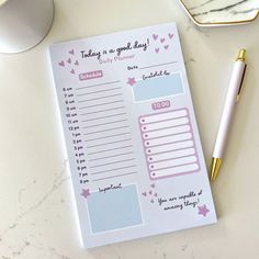 a pink and blue planner next to a pen on top of a white countertop