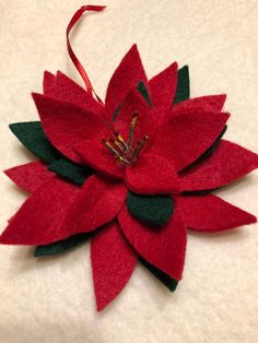 a red poinsettia with green leaves on it's center is sitting on a white surface