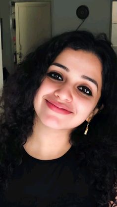 a close up of a person wearing a black shirt and smiling at the camera with long curly hair