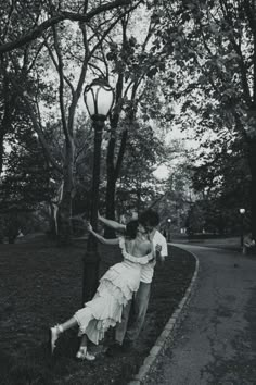 black and white photograph of a couple kissing under a street light in the park with trees