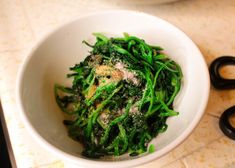 a white bowl filled with green vegetables on top of a counter next to black scissors