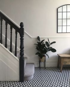 a black and white tiled floor next to a stair case with a potted plant