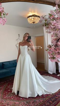 a woman in a white wedding dress taking a selfie with her cell phone and pink flowers