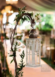 a white lantern hanging from a tree with flowers on it's side at a wedding