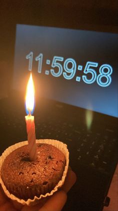 a person holding a cupcake with a lit candle in front of a computer screen