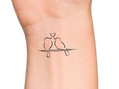 a small tattoo on the wrist of a woman with two birds sitting on a branch