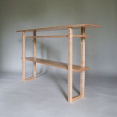 a wooden table with two shelves on each side and one shelf below it, against a gray background