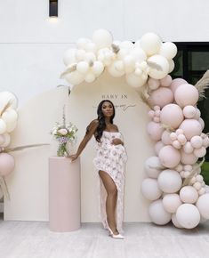 a pregnant woman standing in front of a balloon arch with flowers and balloons on it