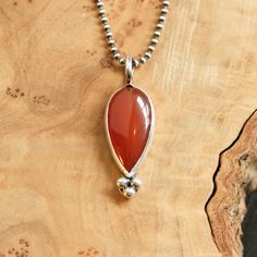 "Such a beautiful color in this burnt orange Carnelian pendant - enhanced by our traditional and delicate \"Sweetheart\" setting with Sterling Silver ball accents. Beautiful Carnelian Pendant - the design seems classic -might be made by a master silversmith from another time - maybe it came from the Mediterranean, given the high-quality semi-precious stone. An upsidedown Carnelian pear or teardrop gemstone at its heart - accented and set in sterling silver - it is so timeless! A traditional but Spiritual Teardrop Cabochon Necklace, Spiritual Teardrop Carnelian Jewelry, Red Garnet Jewelry, Red Pendant, Orange Carnelian, Carnelian Necklace, Red Pendants, Rainbow Moonstone Pendant, Carnelian Pendant