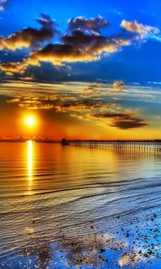 the sun is setting over the ocean with clouds in the sky and water on the beach